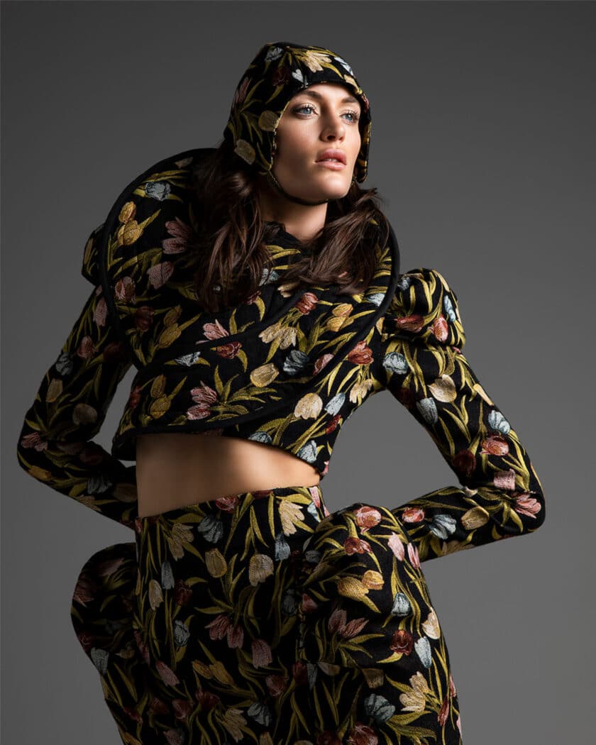 Person wearing a floral-patterned outfit with a matching hat, perfect for any fashion portfolio. The ensemble features puffed sleeves and an exaggerated shoulder design against a grey background.