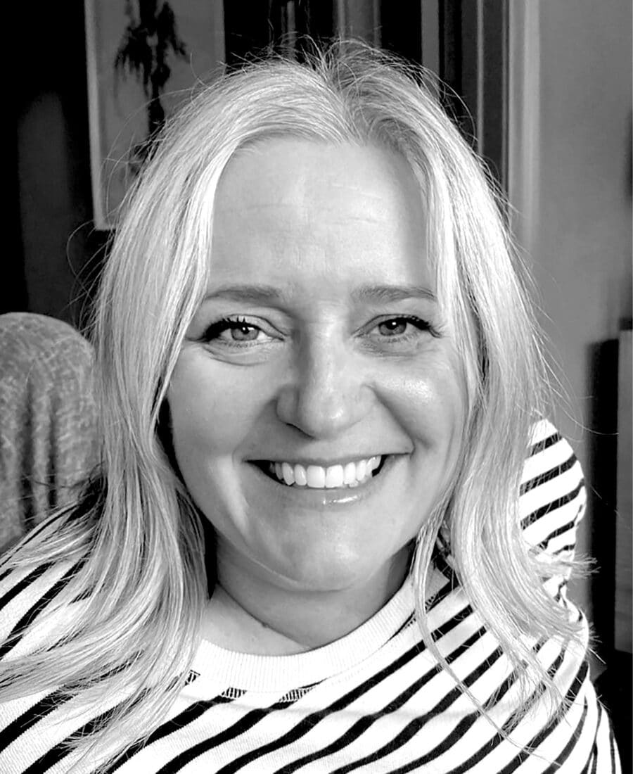 A person with long, light-coloured hair, wearing a striped shirt, smiles at the camera in a black-and-white photo reminiscent of classic style, perfect for an online fashion course.