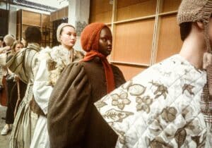 Models lined up backstage at Graduate Fashion Week 2024 wearing layered, textured garments with knitted head coverings, preparing for a fashion show.