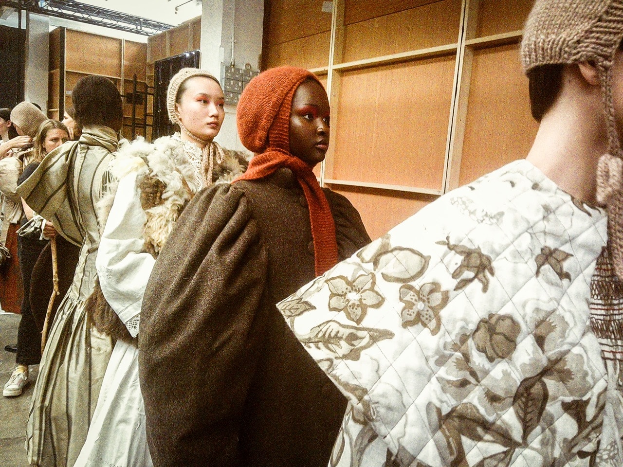 Models lined up backstage at Graduate Fashion Week 2024 wearing layered, textured garments with knitted head coverings, preparing for a fashion show.