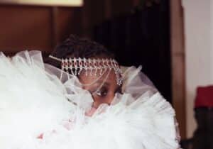 Model wearing a large, ruffled white and red garment adorned with intricate head jewellery.