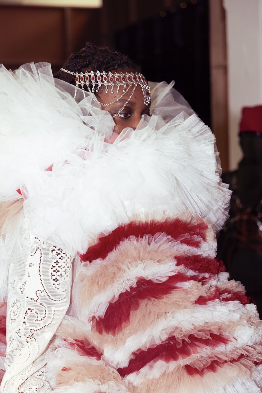 Model wearing a large, ruffled white and red garment adorned with intricate head jewellery.