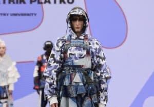 A model on a runway wearing a multi-layered outfit featuring a mix of camouflage and patchwork denim patterns.