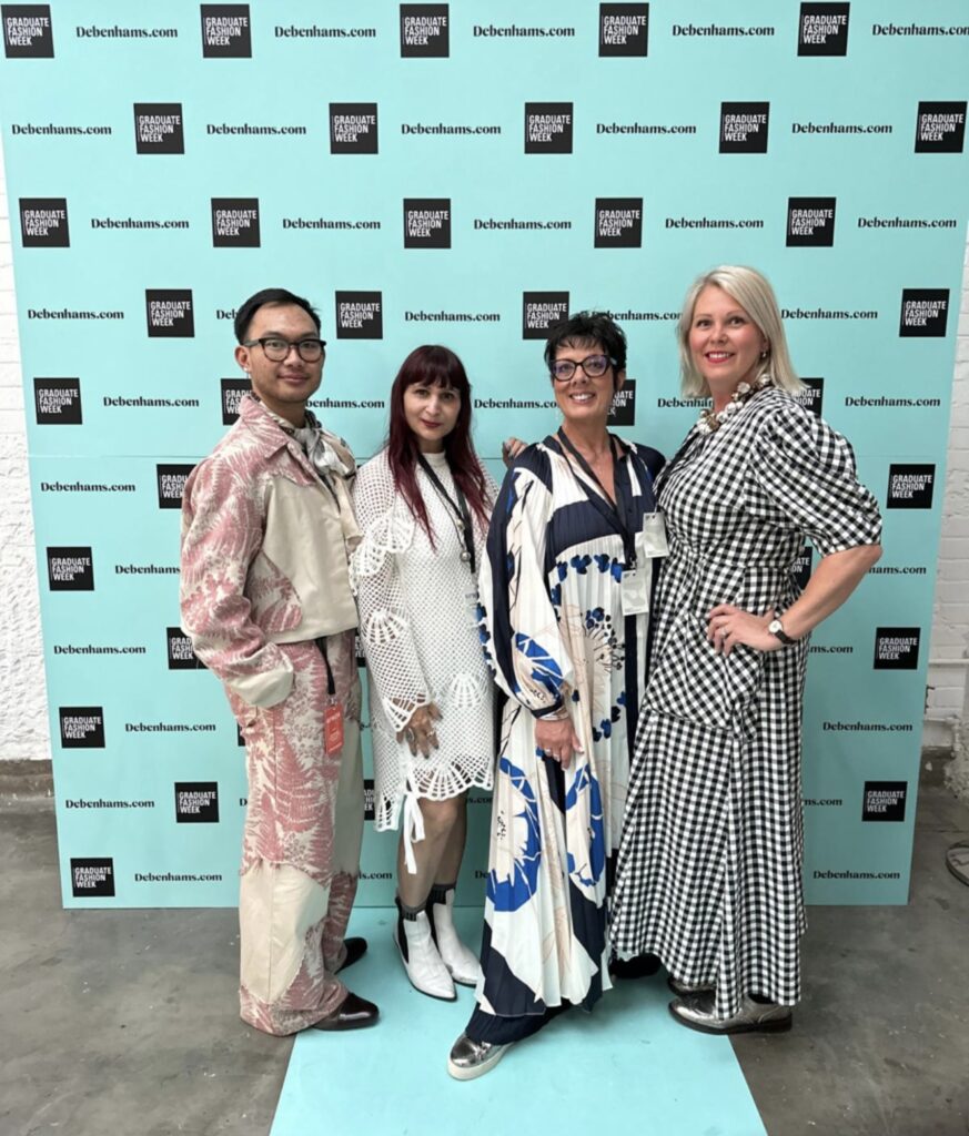 Four individuals in stylish, diverse outfits stand in front of a step-and-repeat banner with "debenhams.com" written on it.