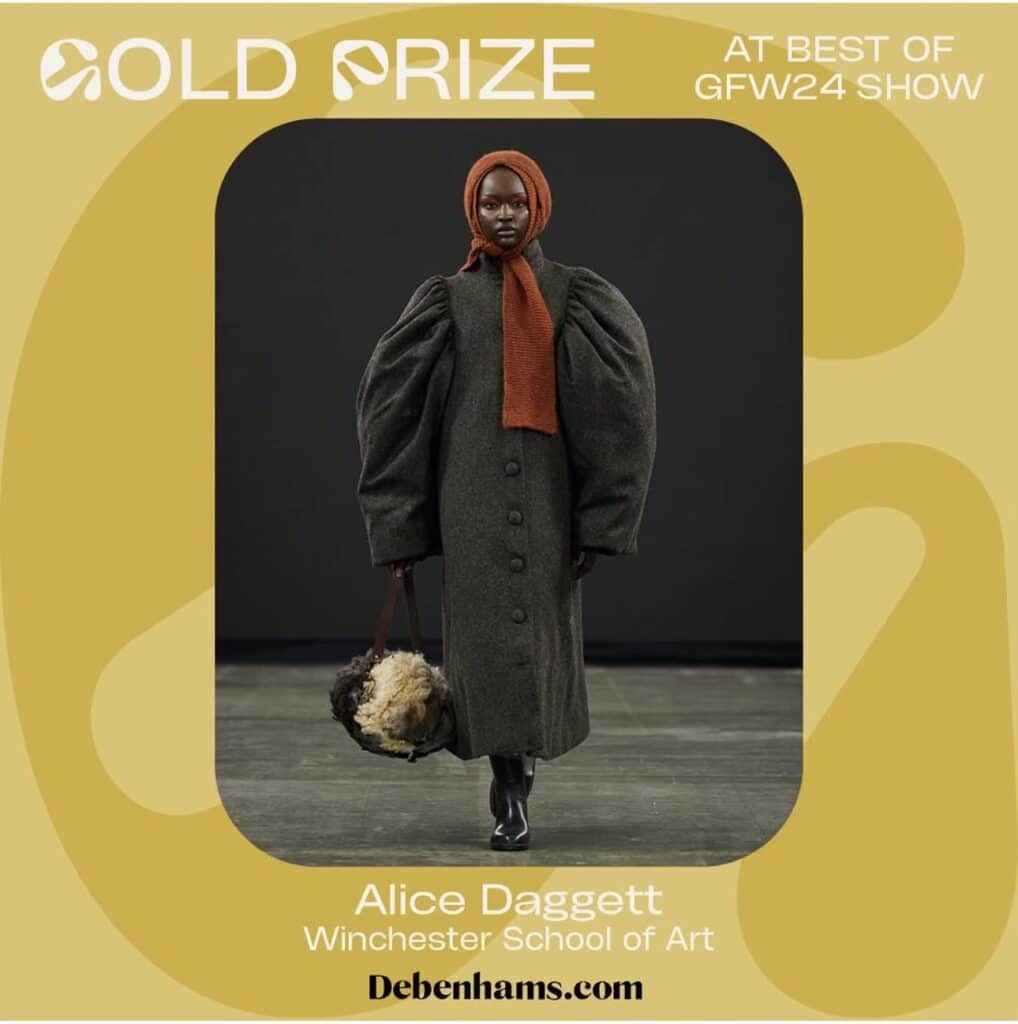 A model wears a dark, long coat with puff sleeves and a rust-coloured scarf. She's holding a furry accessory. Text reads "Gold Prize, Best of GFW24 Show, Alice Daggett, Winchester School of Art, Online Fashion Courses at debenhams.com".