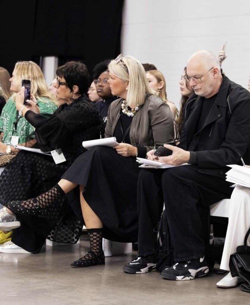 Audience members at a fashion show, seated and focused, with some taking notes and photos, could be seen sharing insights on Graduate Fashion Week 2024.