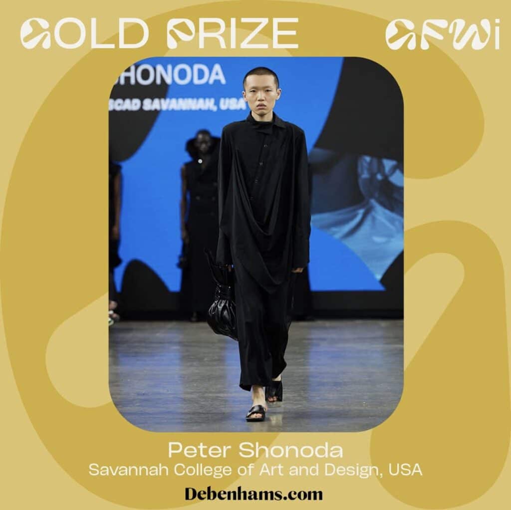 A model walks the runway in a long, black outfit during Graduate Fashion Week 2024. The backdrop showcases text indicating "Gold Prize" awarded to Peter Shonoda from Savannah College of Art and Design, USA.