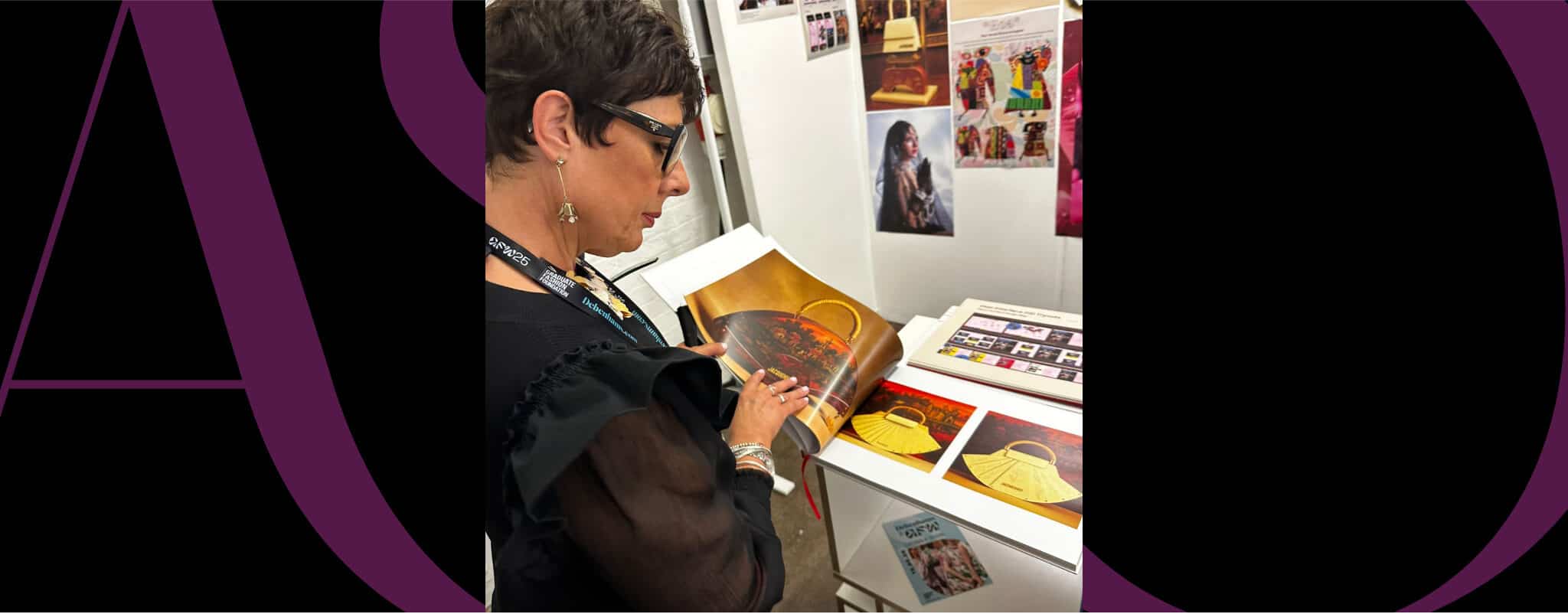 A person wearing glasses examines a print or illustration at a display table with various colorful images and books.