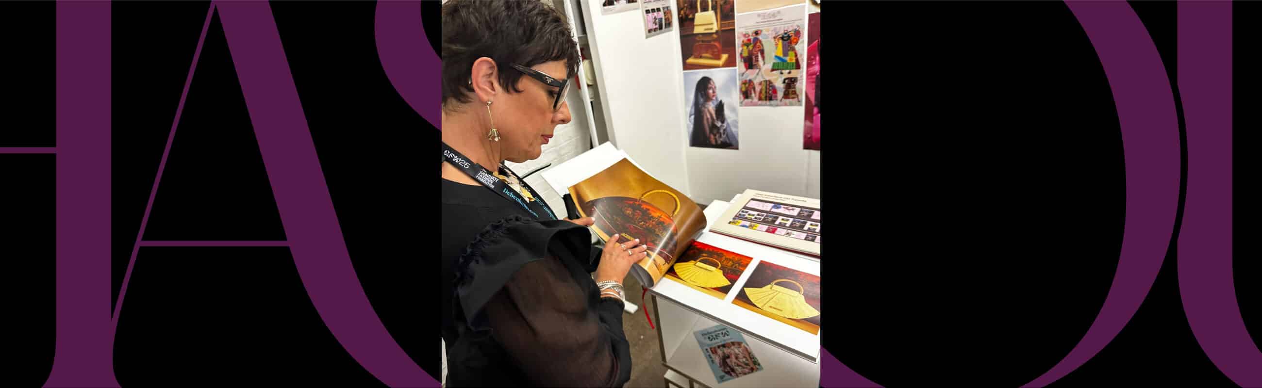A person wearing glasses examines a print or illustration at a display table with various colorful images and books.