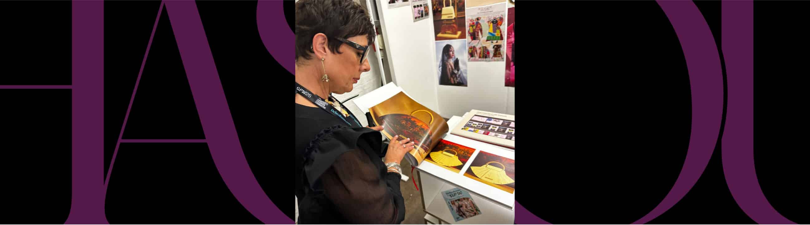 A person wearing glasses examines a print or illustration at a display table with various colorful images and books.