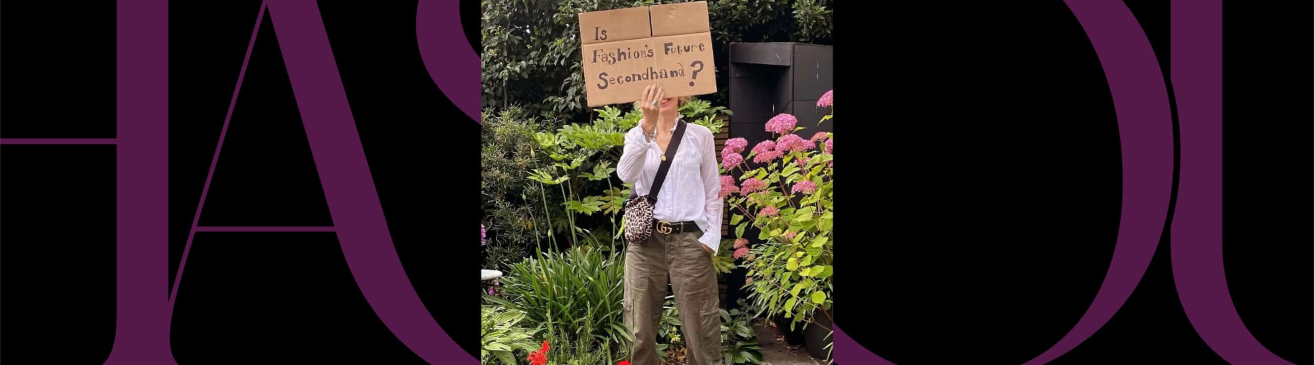 A person stands in a garden holding a cardboard sign that reads, "Is Fashion's Future Sustainable?" Pink flowers and greenery are visible in the background.