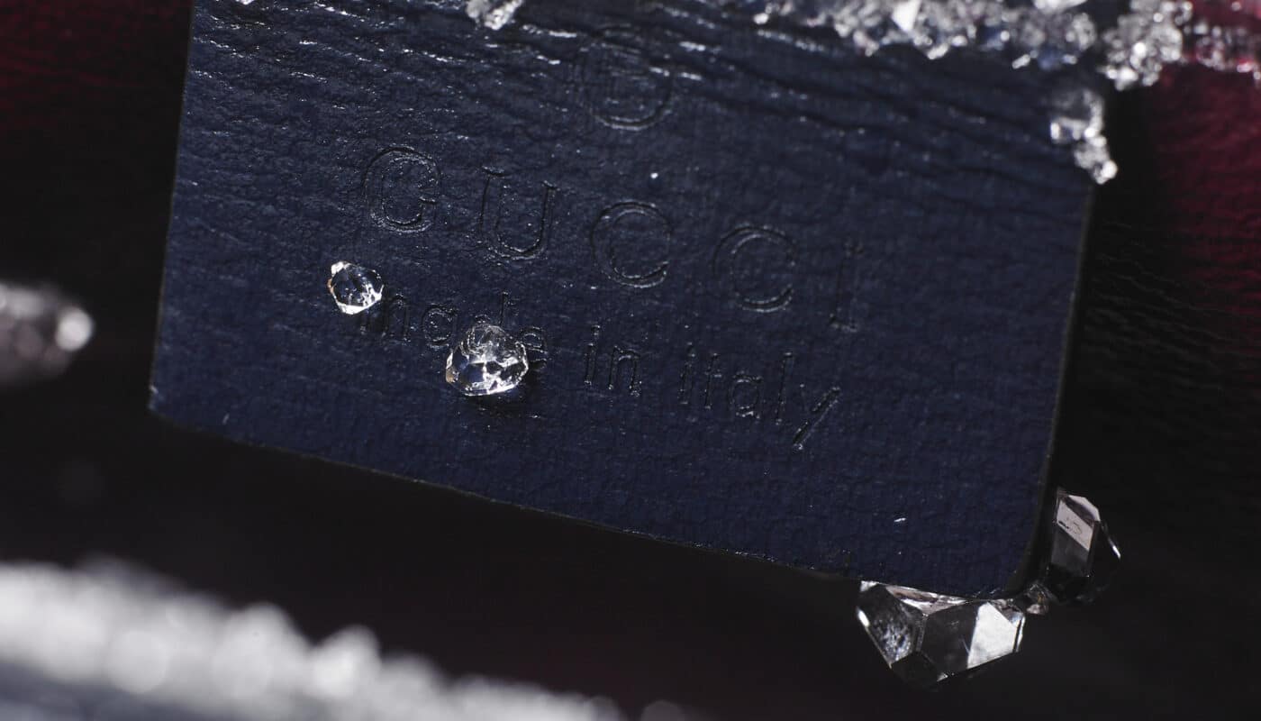 Close-up of a Gucci label that reads "Made in Italy," partially covered with ice crystals and positioned near a gold zipper.