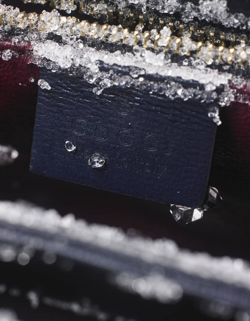 Close-up of a Gucci label that reads "Made in Italy," partially covered with ice crystals and positioned near a gold zipper.